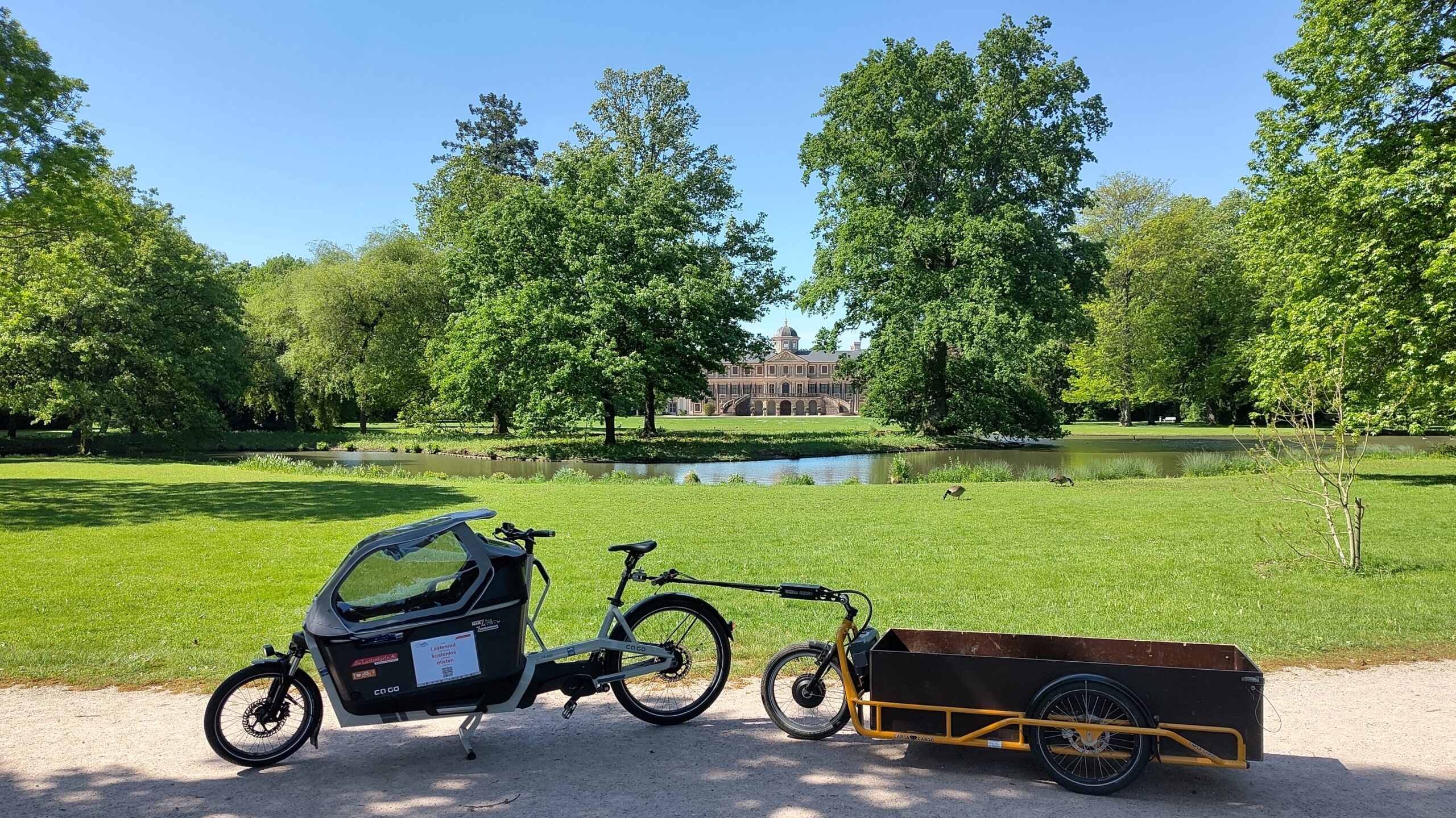 Das Gespann steht im Schlosspark Favorite vor dem Teich und Bäumen. In der Ferne im Bildzentrum das Schloss.